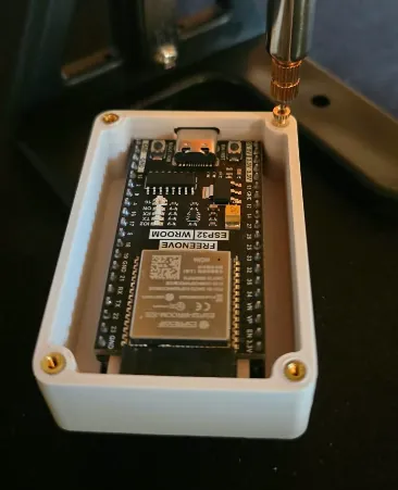 Involucro bianco stampato in 3D con una scheda di sviluppo ESP32-WROOM all'interno e inserti filettati in ottone agli angoli