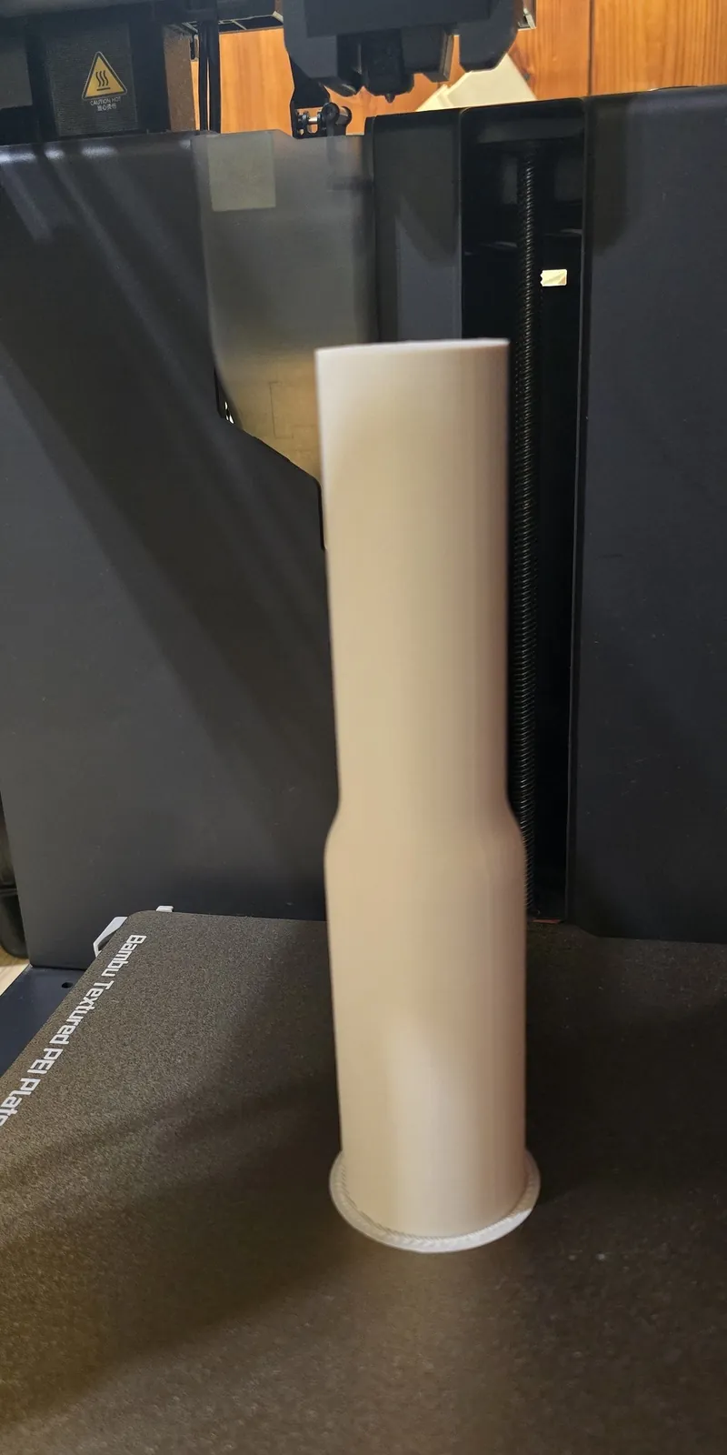 The white PLA extension standing upright on the textured build plate of the 3D printer, with its brim